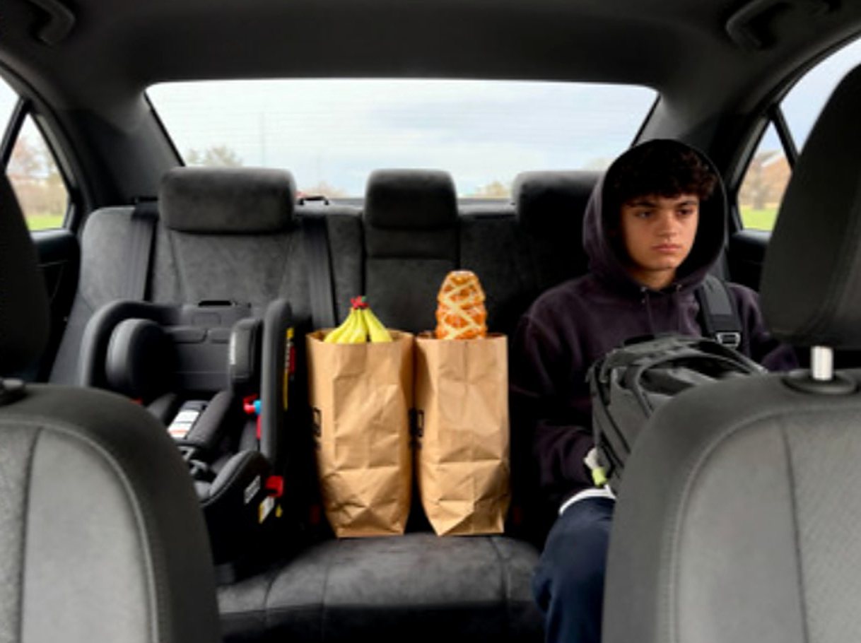 Teen in a back seat beside grocery bags and a child seat